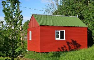 a red house with a green roof in a field at Lauku namiņš - Country cottage in Vecpiebalga