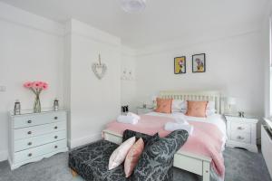 ein weißes Schlafzimmer mit einem rosa Bett und einem Stuhl in der Unterkunft Sea Salt Cottage - Mins to beach & shops Dog Friendly in Deal