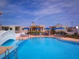 a large swimming pool with chairs and blue umbrellas at Kalimera Hotel in Agia Marina Nea Kydonias