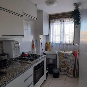a white kitchen with a sink and a stove at Apartamento com varanda - Sahy in Mangaratiba