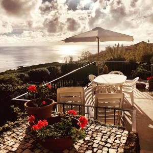 a patio with a table and chairs and an umbrella at Quinta Do Sol Poente in Feteiras