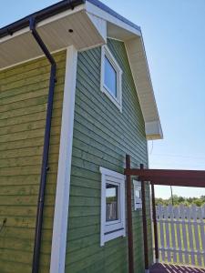 a green house with a porch and a roof at Domki u Iwonki -brązowy in Niechorze +2 photos