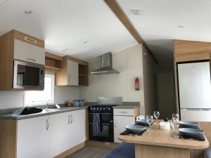 a kitchen with white cabinets and a table with wine glasses at Exclusive 3 Bedroom Caravan, Sleeps 8 People at Parkdean Newquay Holiday Park, Cornwall, UK in Newquay Bay Resort