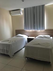 two beds in a hotel room with a window at Ilha Bela Hotel in Paulo Afonso