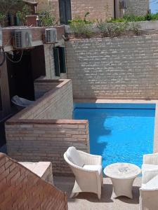 a swimming pool with two chairs and a table next to a brick wall at 2B equipped basement chalet with 2 beds pool view green beach villa 114b in El Alamein