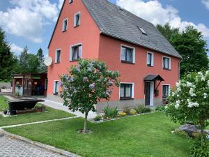 a red house with a tree in the yard at Ferienwohnung Lippmann in Großhartmannsdorf