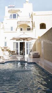 a swimming pool with an umbrella in front of a building at Mood Farmhouse B&B in Għarb