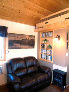 un sofá de cuero en una sala de estar con estantería. en Prairie Rose Cottage, en Fort Macleod
