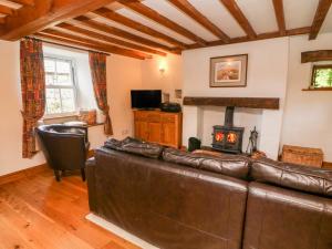 a living room with a leather couch and a fireplace at Spout Cottage in Sedbergh