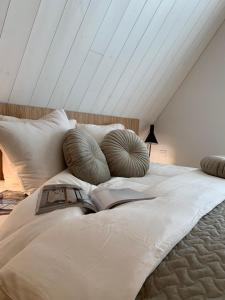 Una cama blanca con almohadas y un libro. en Aurora apartments, en Palanga