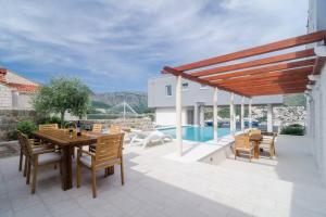 patio z drewnianym stołem i krzesłami oraz basenem w obiekcie Modern Villa with Swimming Pool - Penthouse w Dubrowniku