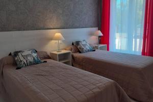 two beds in a hotel room with red curtains at appartement 4 pers dans longère à 800m de la plage in Plouhinec