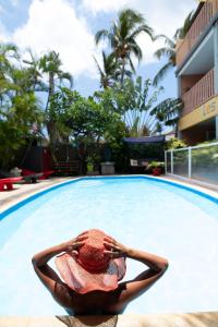 a woman in a hat sitting in front of a swimming pool at Hôtel les Bougainvilliers in Saint-Gilles les Bains
