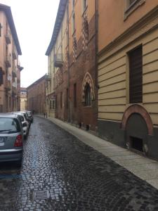 una calle adoquinada con coches estacionados al lado de un edificio en centro storico Asti Monferrato Langhe, en Asti