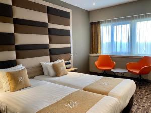 a hotel room with two beds and orange chairs at XO Hotels Blue Tower in Amsterdam