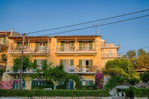 un grande edificio giallo con balconi e alberi di MANESSIS Apartments Kassiopi Bay Corfu a Kassiopi