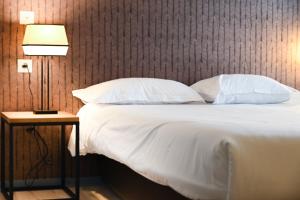 a bed with white sheets and pillows and a lamp at Hôtel Les Muses in Annecy
