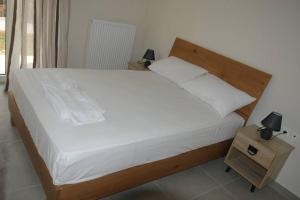 a bed with white sheets and a wooden headboard and a night stand at lividio apartment in Lefkada