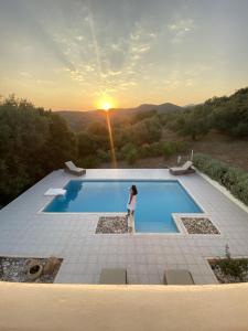 une femme debout à côté d'une piscine avec le coucher du soleil dans l'établissement Kyparissia De Wandelboom, à Vrísai