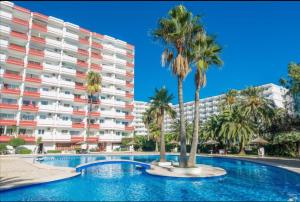 a swimming pool with palm trees in front of a building at Apartamento Laura in Alcudia