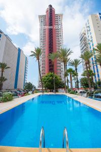 a large blue swimming pool in front of a tall building at Las Damas Premium 23F Beach Front - Pool & Parking in Benidorm