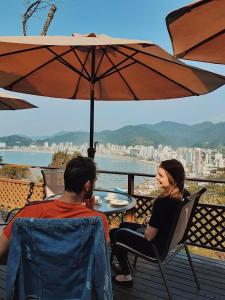 un hombre y una mujer sentados en una mesa bajo un paraguas en Hotel Pousada 7 Mares, en Itapema
