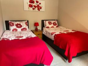 two beds in a bedroom with red and white sheets at Derrybrook Cottage, Twin or Superking, Seven Springs Cottages in Cheltenham