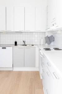 a white kitchen with white cabinets and a wooden floor at Apartment Sleepwell, Leppävaara, 71m2 with private sauna in Espoo