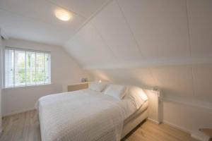 a white bedroom with a bed and a window at Sous les Dunes in Schoorl