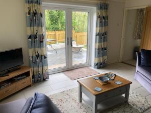 ein Wohnzimmer mit einem Sofa, einem Tisch und einer Glasschiebetür in der Unterkunft Sycamore Bungalow in Perranwell