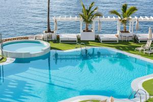 a pool with chairs and the ocean in the background at Hotel LIVVO Puerto de Mogán in Puerto de Mogán