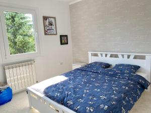 a bedroom with a bed with a blue comforter and a window at LA CASITA Serbia in Surčin