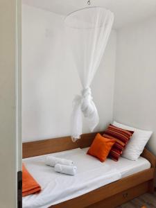 a bed with orange and white pillows and a curtain at Villa Dora - Mediterranean family house for 9 with private garden, BBQ, sea view and private parking for 4 cars in Pag