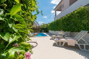 een patio met een zwembad, stoelen en planten bij Apartments Orlic in Trogir