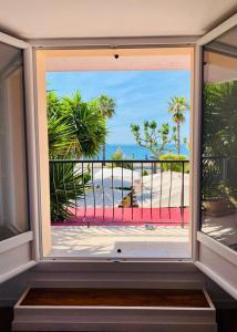 a window with a view of a beach with palm trees at Maison de la Marine in Cagnes-sur-Mer