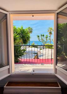 a window with a view of a beach with palm trees at Maison de la Marine in Cagnes-sur-Mer