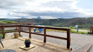 a wooden deck with a bench and mountains in the background at Achmelvich View self catering in Lochinver