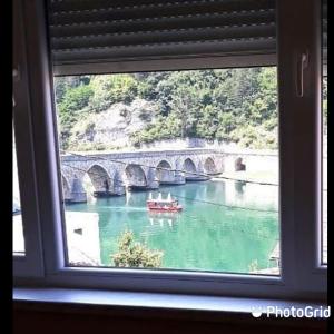 a window view of a bridge and a boat in the water at Apartman Trg Višegrad in Višegrad