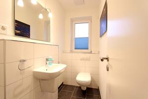 a white bathroom with a toilet and a sink at Merlin 3 Waldstr 20 h in Kellenhusen +4 photos