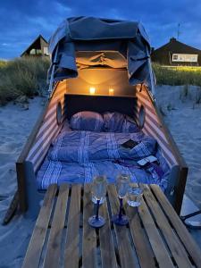 ein Bett in einem Boot am Strand mit zwei Gläsern in der Unterkunft Schlafstrandkorb Nr. 3 in Sierksdorf