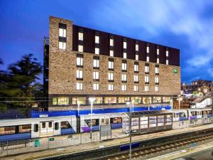 a train at a train station with a building at ibis Styles London Seven Kings in Ilford