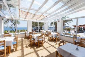 un restaurante con mesas y sillas blancas y el océano en Kinira Beach Hotel en Kinira