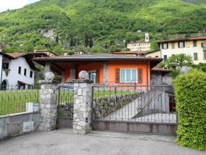 ein orangenes Haus mit einem Zaun vor einem Berg in der Unterkunft Villa Lenno by Interhome in Lenno
