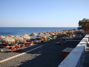 a beach area with tables, chairs and umbrellas at Marousi Rooms in Perissa