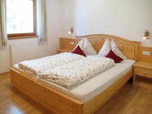 a wooden bed with red and white pillows on it at Apartment Obermüllerhof-1 by Interhome in Maranza