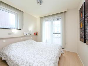 a white bedroom with a bed and two windows at Apartment Cocoon with parking by Interhome in Bredene