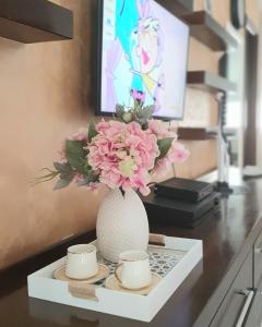 a vase with pink flowers on a table with two cups at Apartman Anja in Budva