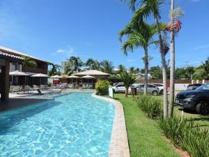 a swimming pool at a resort with palm trees and cars at Itacimirim - Village na Praia da Espera in Itacimirim