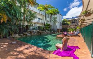 a woman in a pink dress sitting next to a swimming pool at Coral Tree Inn in Cairns