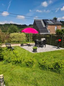 eine Terrasse mit einem rosa Regenschirm, einem Tisch und Stühlen in der Unterkunft Ké dodo sous le château !!! in Spa